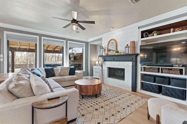 living room featuring light wood-style floors, a tiled fireplace, crown molding, and a textured ceiling