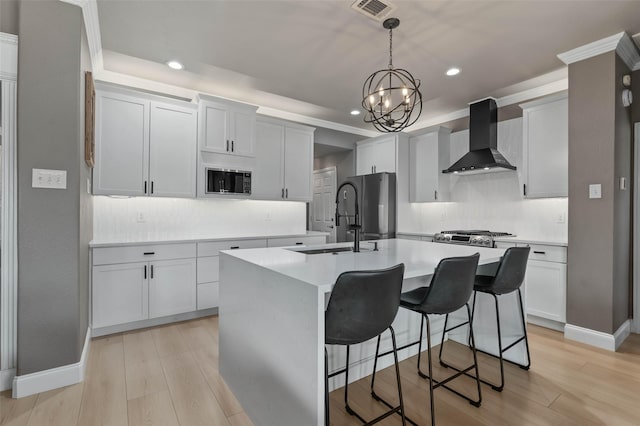 kitchen featuring light countertops, a kitchen island with sink, light wood finished floors, and wall chimney exhaust hood