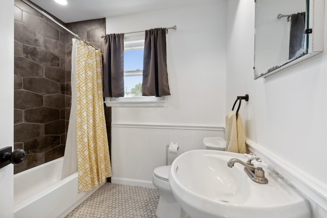 bathroom with toilet, a wainscoted wall, a sink, tile patterned floors, and shower / bath combo with shower curtain