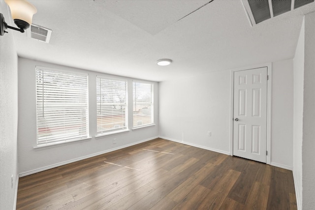 spare room with dark wood-style flooring, visible vents, and baseboards