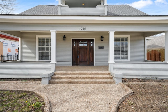 doorway to property with covered porch and a shingled roof