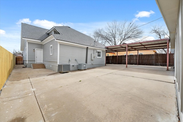 exterior space with entry steps, roof with shingles, fence private yard, cooling unit, and a carport