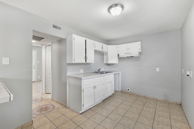 kitchen featuring tile countertops, under cabinet range hood, white cabinetry, and visible vents