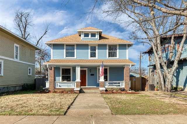 traditional style home featuring covered porch, fence, a front lawn, and brick siding