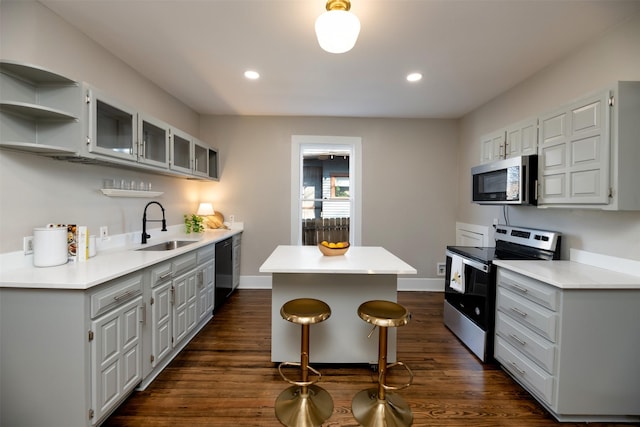 kitchen with dark wood-type flooring, a kitchen island, a sink, baseboards, and appliances with stainless steel finishes