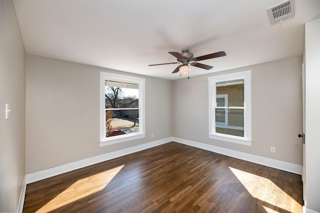 spare room with dark wood-type flooring, visible vents, ceiling fan, and baseboards