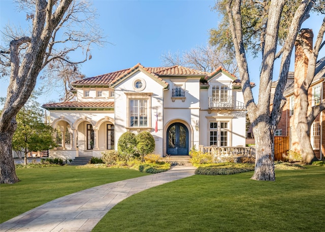 mediterranean / spanish home featuring a balcony, a tile roof, french doors, stucco siding, and a front yard