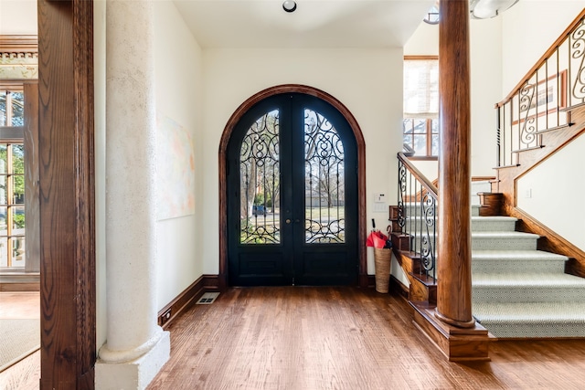 foyer featuring arched walkways, wood finished floors, french doors, stairway, and decorative columns