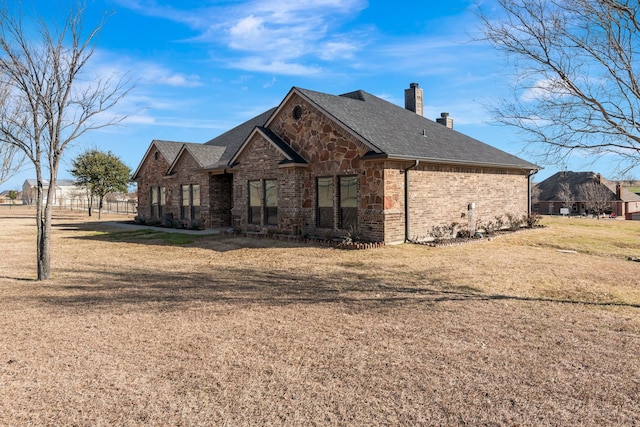 view of property exterior featuring brick siding, roof with shingles, a chimney, a lawn, and stone siding