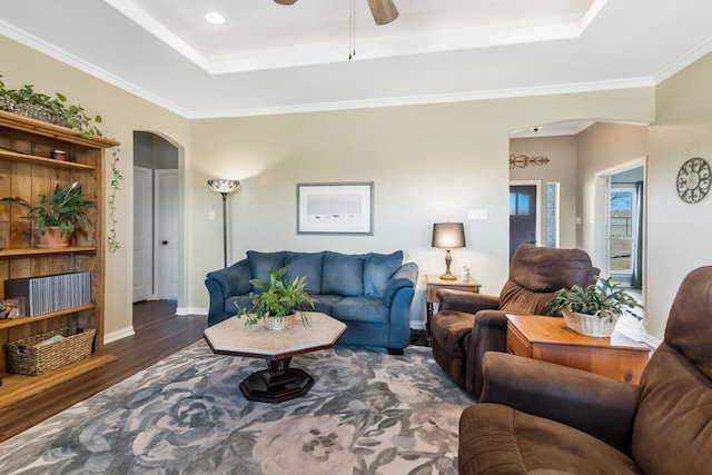 living area with arched walkways, a tray ceiling, crown molding, wood finished floors, and baseboards