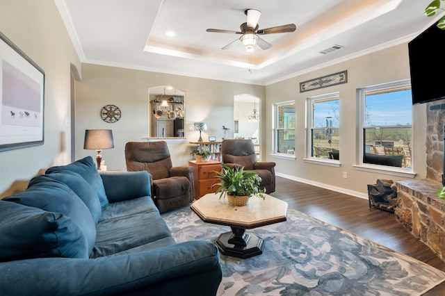 living room featuring ceiling fan with notable chandelier, wood finished floors, visible vents, ornamental molding, and a tray ceiling