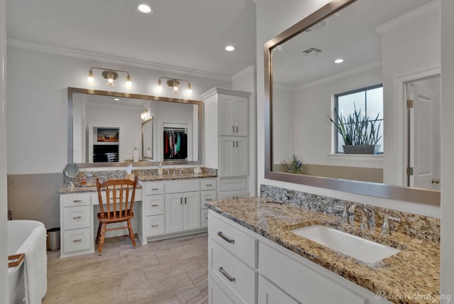 bathroom featuring ornamental molding, a sink, a freestanding bath, two vanities, and recessed lighting