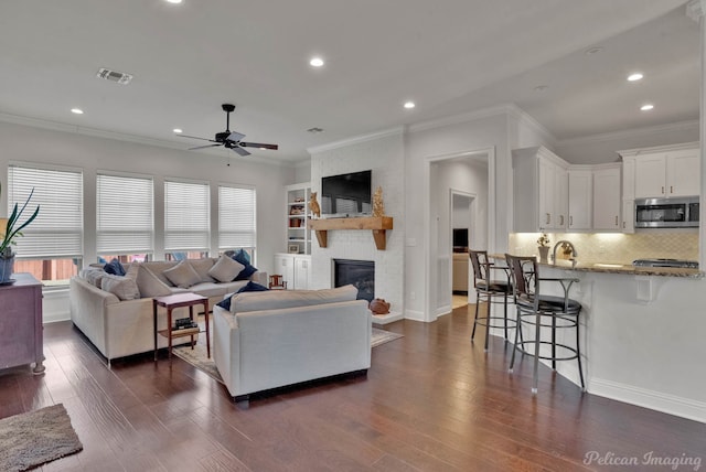 living room featuring ornamental molding, a fireplace, dark wood finished floors, and visible vents