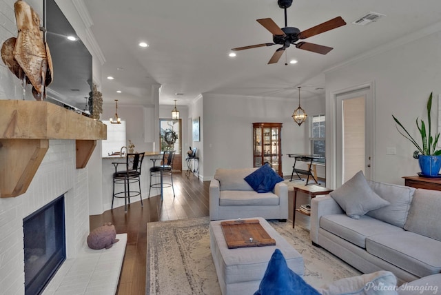 living area featuring a brick fireplace, visible vents, wood finished floors, and ornamental molding