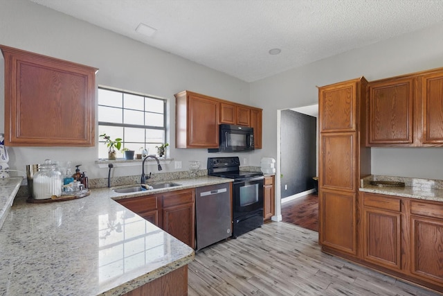 kitchen featuring black appliances, light wood-style flooring, brown cabinetry, and a sink