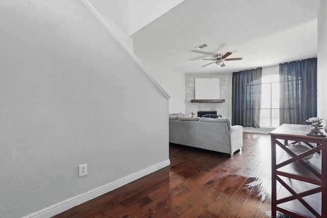 living room with a fireplace, dark wood finished floors, visible vents, a textured ceiling, and baseboards