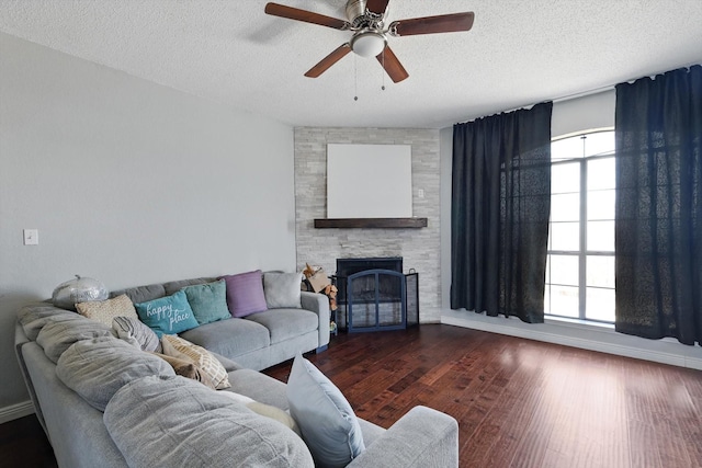 living room featuring a stone fireplace, a textured ceiling, baseboards, and wood finished floors