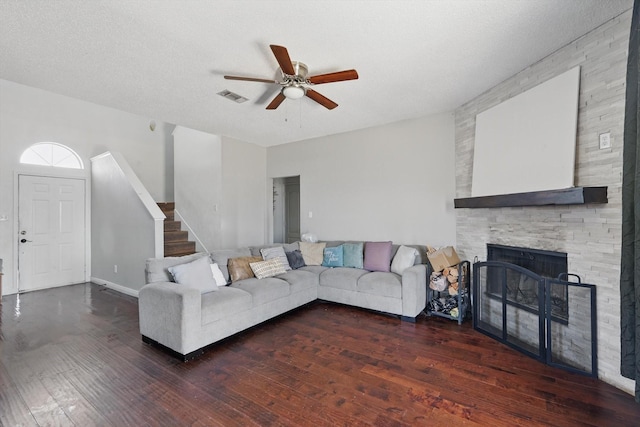 living room with visible vents, hardwood / wood-style flooring, ceiling fan, stairway, and a stone fireplace