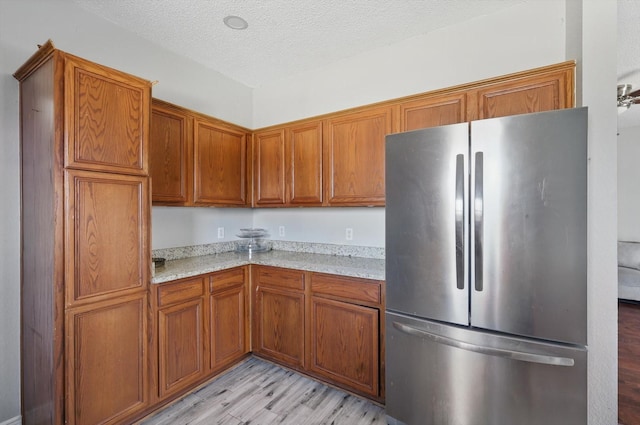 kitchen featuring brown cabinetry, a textured ceiling, and freestanding refrigerator