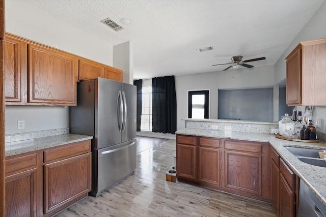 kitchen with stainless steel appliances, brown cabinetry, visible vents, and a peninsula