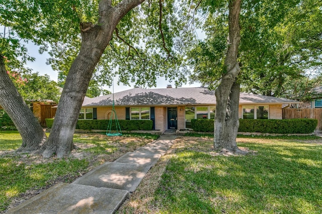 ranch-style home featuring brick siding, a shingled roof, fence, a front lawn, and a chimney