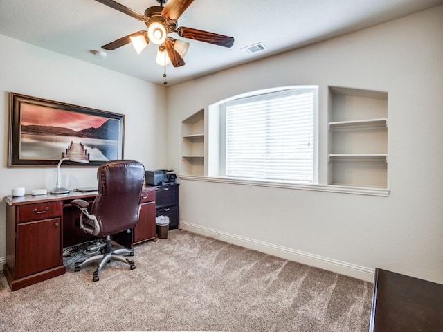 office area featuring built in shelves, light colored carpet, a ceiling fan, baseboards, and visible vents