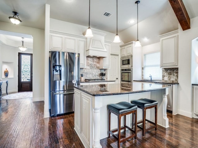 kitchen featuring dark wood-style flooring, visible vents, appliances with stainless steel finishes, a center island, and dark stone countertops