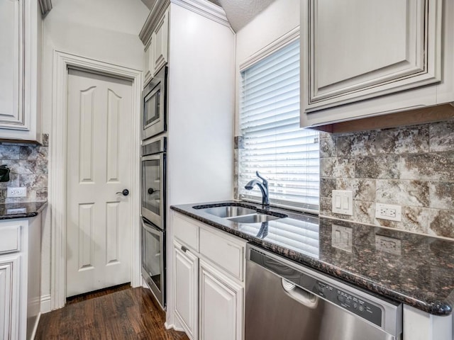 kitchen featuring tasteful backsplash, dark wood-style floors, dark stone countertops, stainless steel appliances, and a sink