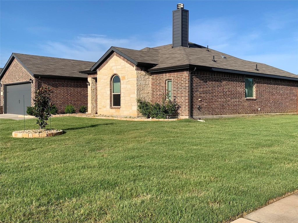 view of side of home with stone siding, a chimney, an attached garage, a yard, and brick siding