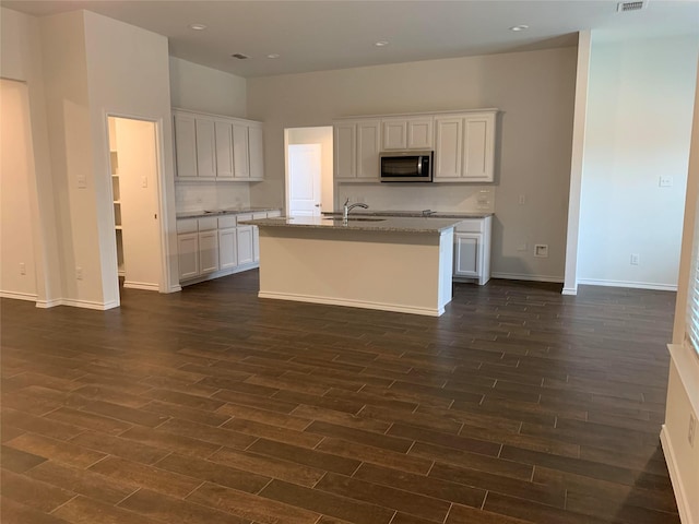 kitchen with white cabinets, stainless steel microwave, dark wood finished floors, and an island with sink