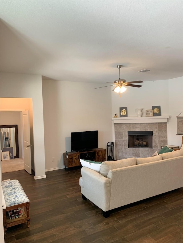 living area with ceiling fan, a fireplace, baseboards, and dark wood-type flooring