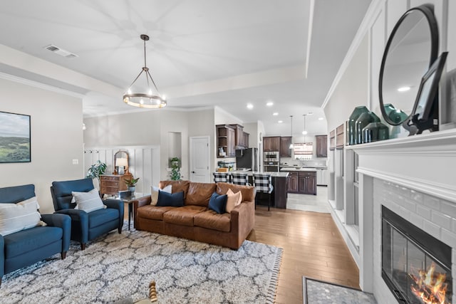 living area featuring ornamental molding, a glass covered fireplace, visible vents, and light wood-style floors