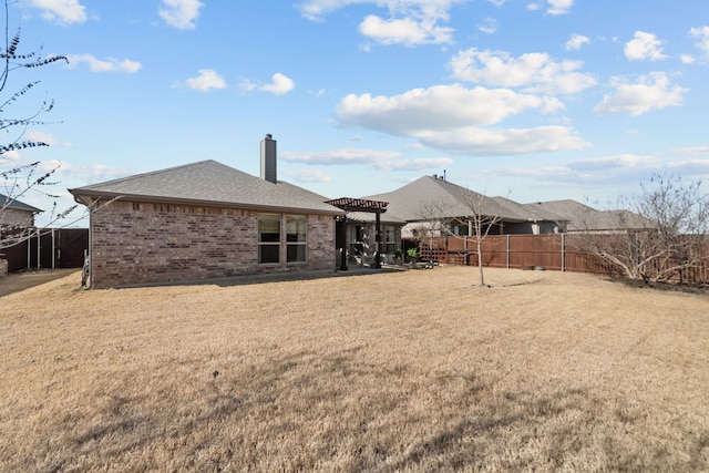 rear view of house featuring brick siding, a yard, a chimney, roof with shingles, and a fenced backyard