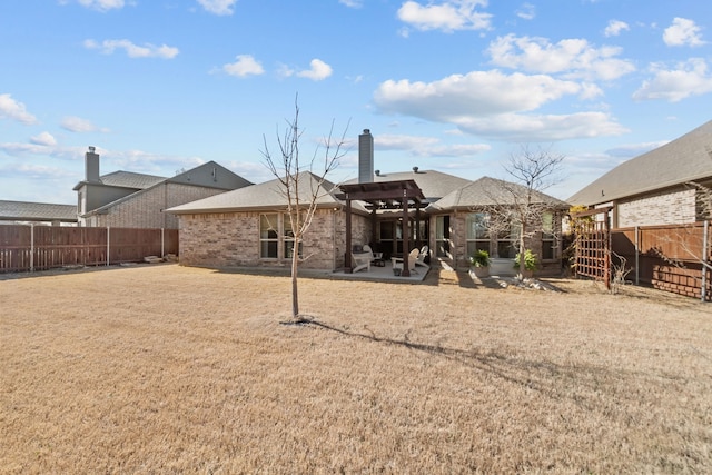 back of property featuring a fenced backyard, brick siding, a yard, a chimney, and a patio area