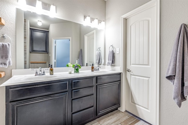 bathroom featuring double vanity, wood finished floors, a sink, and a textured wall