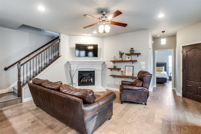 living area with recessed lighting, wood finished floors, baseboards, stairway, and a glass covered fireplace