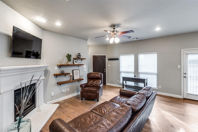 living room featuring a fireplace, visible vents, ceiling fan, wood finished floors, and baseboards