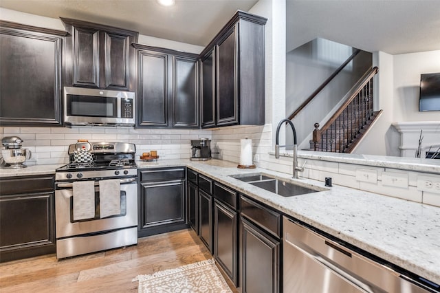 kitchen with light stone counters, decorative backsplash, appliances with stainless steel finishes, a sink, and light wood-type flooring