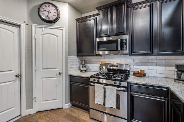 kitchen with a textured wall, light stone counters, wood finished floors, stainless steel appliances, and backsplash