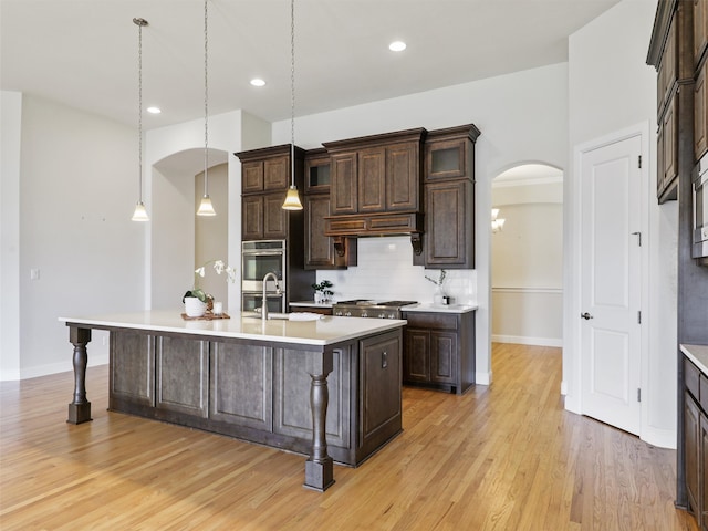 kitchen featuring arched walkways, light countertops, stainless steel double oven, and dark brown cabinetry