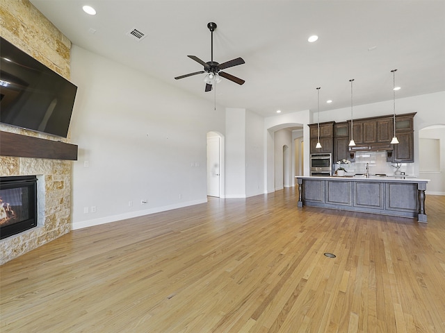 unfurnished living room featuring visible vents, arched walkways, ceiling fan, light wood-style flooring, and a fireplace