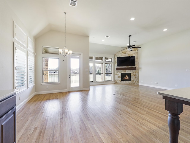 unfurnished living room with lofted ceiling, light wood-style flooring, ceiling fan with notable chandelier, a fireplace, and visible vents