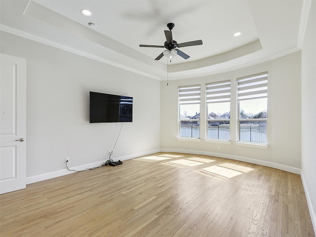 unfurnished living room with light wood finished floors, a tray ceiling, and baseboards