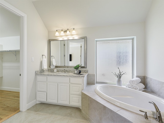 full bath featuring tile patterned flooring, a garden tub, vanity, baseboards, and a spacious closet