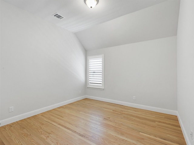 empty room featuring light wood-style floors, baseboards, visible vents, and vaulted ceiling