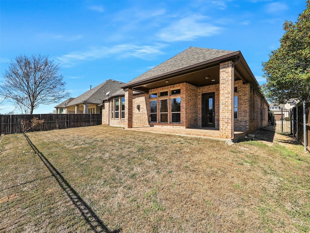 back of property featuring brick siding, a lawn, a fenced backyard, and roof with shingles