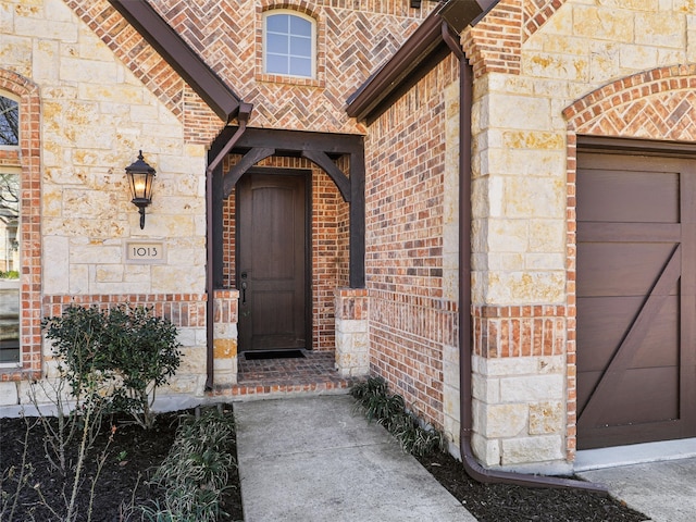 doorway to property featuring an attached garage, stone siding, and brick siding