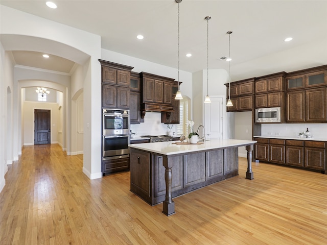 kitchen featuring arched walkways, stainless steel appliances, dark brown cabinets, and light countertops