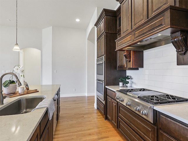 kitchen featuring arched walkways, stainless steel appliances, light wood-style floors, a sink, and premium range hood