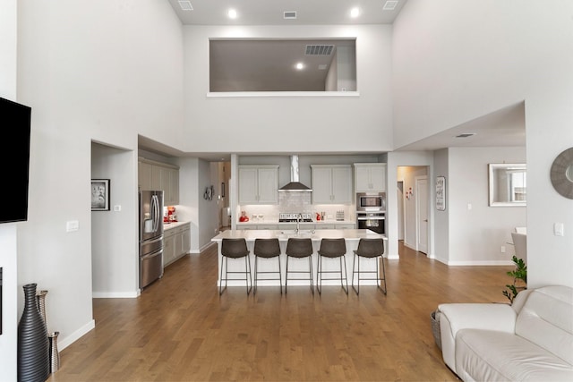 kitchen with stainless steel appliances, light countertops, a sink, wall chimney range hood, and a kitchen bar